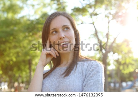 Pensive happy adult woman looking at side standing in a park