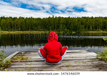girl in red sitting on the background of a forest lake
