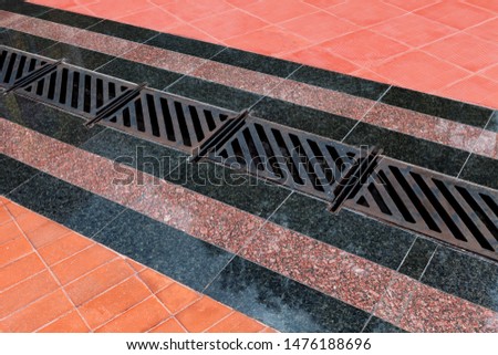 Pedestrian covering, lined with granite tiles with metal drainage grate. Sidewalk drainage system