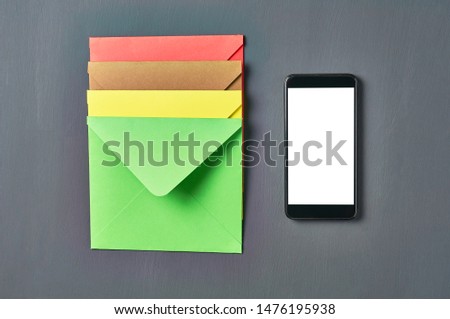 Black smartphone with isolated white screen near row of colorful square envelopes lies on old scratched dark concrete. Top view