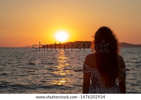 Silhouette of woman relaxing against sunset . Girl on pontoon pier at sunset . Woman relaxing on pier looking at sea view at sunset. 
