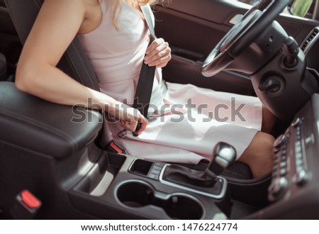 girl driving car, in summer in city, fastens her seat belt, latches lock. View of interior of car close-up steering wheel. Girl in a dress, automatic transmission, armrest and cup holders background Royalty-Free Stock Photo #1476224774