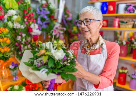 Smiling portrait of an attractive florist business woman owner at a flower shop market working and making a new floral arrangement during a sunny day. Small business owner.