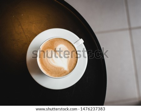 One cup of cappuccino with latte art on black table, white ceramic cup, top view. Cafe culture.
