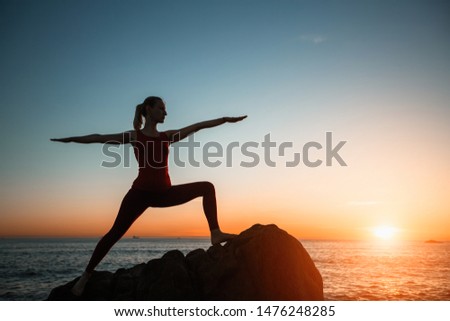 Silhouette of yoga woman doing exercise on the sea beach during amazing surreal sunset. 