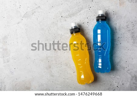 Isotonic energy drink. Bottle with blue and yellow transparent liquid, sport beverage on a gray concrete background. It usually contains salt and sugar and maintains optimal hydration Royalty-Free Stock Photo #1476249668