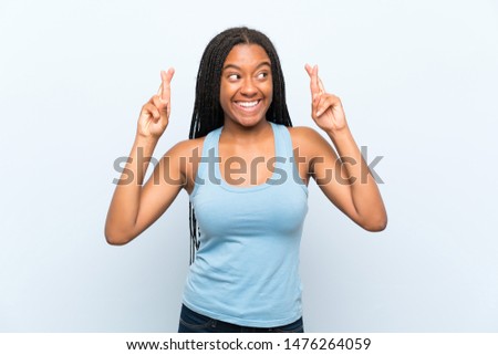 African American teenager girl with long braided hair over isolated blue background with fingers crossing
