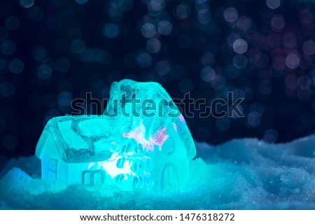 Glowing toy house in the snow on the background of Christmas lights. Festive, Christmas or New Year concept