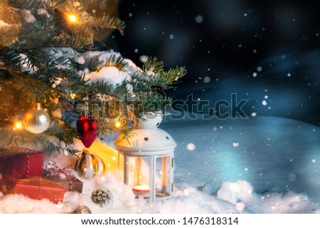 Christmas composition - gifts and a lantern in the snow under a Christmas tree decorated with lights and Christmas-tree decorations, copy space, place for text