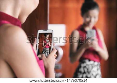 Mirror selfie woman taking picture with mobile phone in store mirror shopping for clothes looking at her fashion oufit for office taking selfies in changing room. Weight loss, body image, self-esteem.