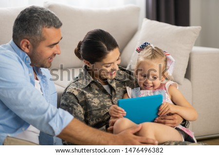 Unbelievably happy. Military woman feeling unbelievably happy watching cartoon with daughter and husband