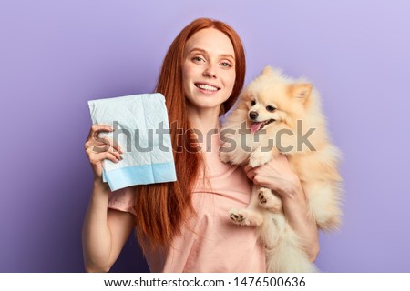 red-haired pretty positive girl controlling pissing process of her pet. close up portrait isolated blue background Royalty-Free Stock Photo #1476500636