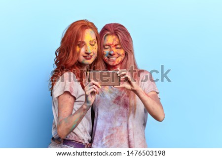 cheerful positive sisters with colourful faces taking a picture on the holiday, close up portrait. isolated blue background, studio shot