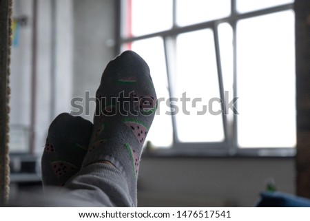 Two feet of a man who is lying on a bed, against the background of a window on a sunny day