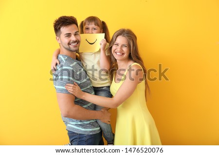 Portrait of happy family with drawn smile on sheet of paper against color background