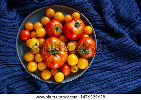 Fresh tomatoes in a plate on a dark blue background. Harvesting tomatoes. Top view. Cherry tomatoes are different varieties in plate, tomatoes of different colors, types and size.
