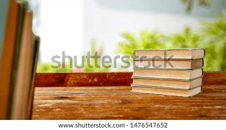 Wooden table background with some books. Blurred green plants in distance. Empty space for products and decoration.