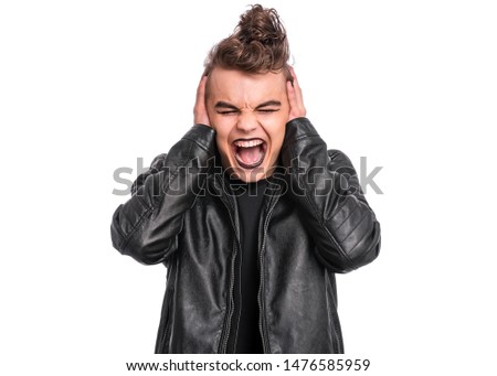 Rebellious teen boy dressed in black, isolated on white background. Young teenager in style of punk goth wearing leather jacket, covers ears by hands and shouting. Problems of transitional age.