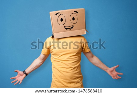 Young man standing and gesturing with a cardboard box on his head with drawn smiley face