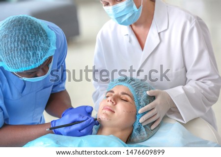 Plastic surgeon applying marks on woman's face before operation in clinic