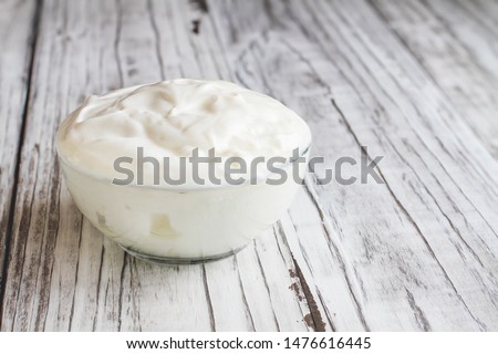 Bowl of plain Greek yogurt over a rustic white wood table background..