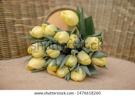 A bouquet of yellow tulips lies on a wicker brown chair opposite the window
