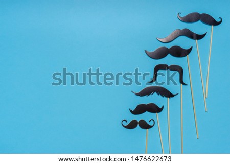 Various black photo booth props moustaches of different shape on blue background. Greeting card, text HAPPY FATHER'S DAY. Flat lay, top view