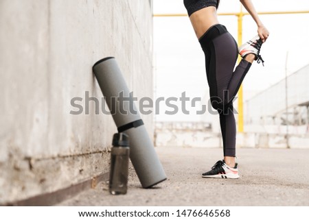 Cropped image of a young fitness girl leaning on a wall while standing outdoors, doing stretching exercises