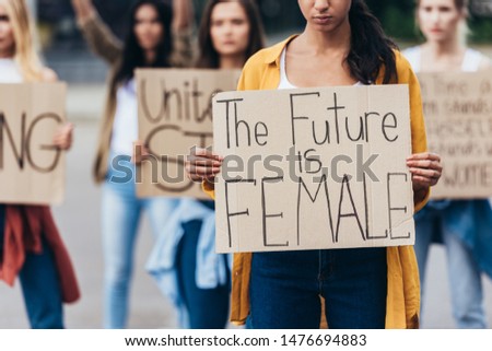 cropped view of girl holding placard with inscription the future is female near feminists on street