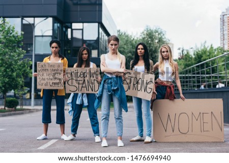 full length view of multiethnic feminists holding placards with slogans on street