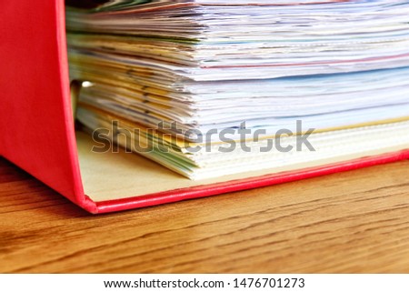 Red ordner with papers. Stack of business papers, bills or documents in ordner document binder closeup on wooden desk. Debt free life, business office stress workload or paperless office concept.    
