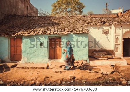 People walking past small traditional indian village house. Colorful buildings of rural area in India. Royalty-Free Stock Photo #1476703688
