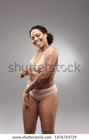 Smiling lady with curly hair wearing light underwear and showing her tattoo. Overweight concept