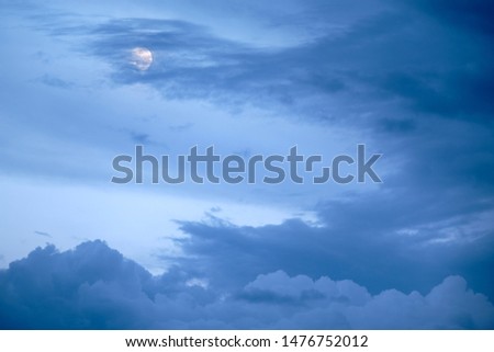 The moon hiding behind some clouds on an dramatic evening sky in summer in Germany