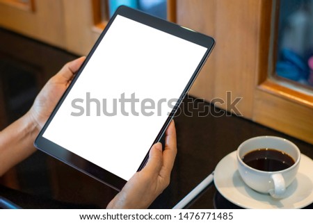 Mockup image of business woman hands holding black tablet computer pc  with blank white screen with pencil and  cup of hot black coffee on table at cafe.