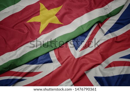 waving colorful flag of great britain and national flag of suriname. macro