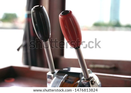Black and red throttle control in boat which made with stainless steel , background is Choa Phraya River.