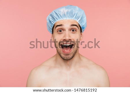 Beauty portrait of an excited handsome shirtless brunette man standing isolated over pink background, wearing shower cap Royalty-Free Stock Photo #1476815192