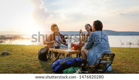 blurry and soft focus of group of Asian friends tourist drinking and playing guitar together with happiness in Summer while having camping near lake at sunset