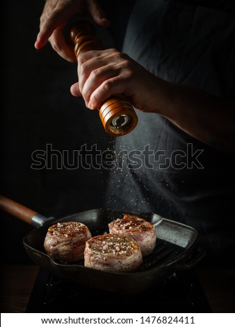 Close up chef hands adding pepper in mill during cooking beef steak on grill pan black background for copy space text restaurant menu,