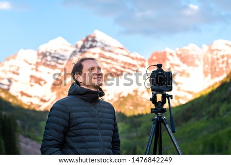 Maroon Bells at sunrise with smiling man photographer and tripod in Aspen, Colorado with rocky mountain peak and snow
