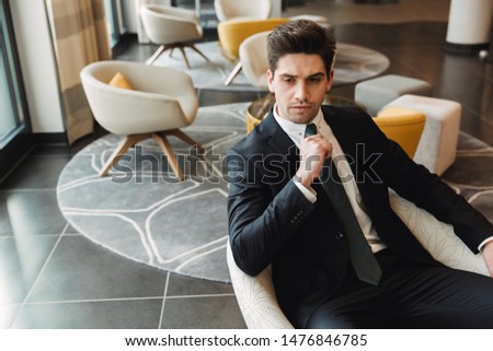 Photo of a young serious businessman indoors in business center office.