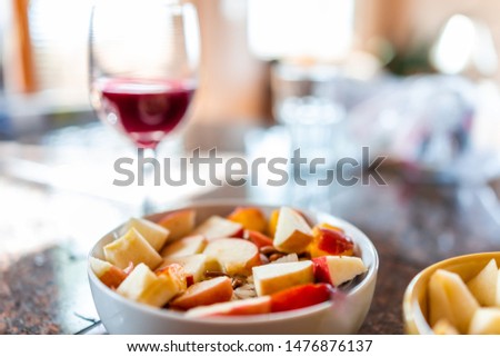 Closeup of colorful bowl with apple and peach slices on porridge with bokeh background of red wine glass on kitchen counter or restaurant