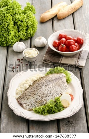 Fried cod on white plate with fresh vegetables and egg, on old wooden table. Tomatoes and other fresh vegetables in the background.