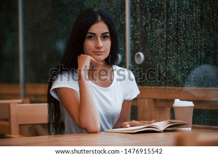 Portrait of young female student that sits in cafe at rainy day. One person only.