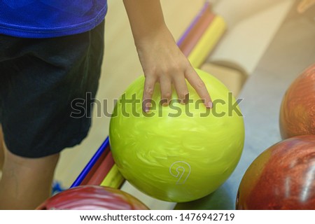Close up hand of children player is holding bowling balls in joyful bowling game.  One kind of fun sport game that have to throw balls to hit ten pins to get score. Happy hobby/competitive activity