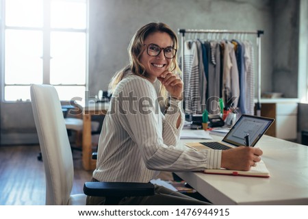 Smiling young woman taking note of orders from customers. Dropshipping business owner working in her office. Royalty-Free Stock Photo #1476944915