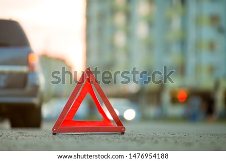 Red emergency triangle stop sign and broken car on a city street.