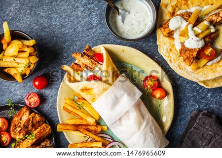 Gyros souvlaki wraps in pita bread with chicken, potatoes and tzatziki sauce, blue background, top view.