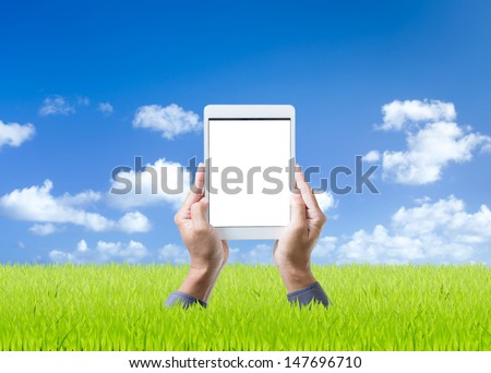 Man hand holding digital tablet on green grass and blue sky background